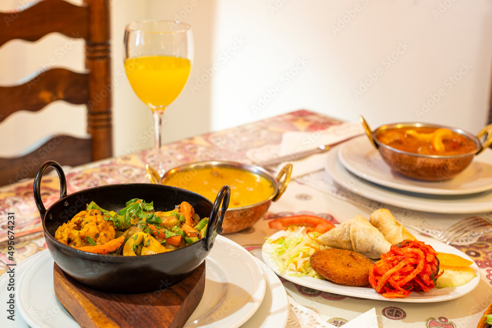 Curry stews and typical appetizers of Indian food in Europe, onion bhaji, cheese roll, samosas, falafel and pickled vegetables on the table in a restaurant