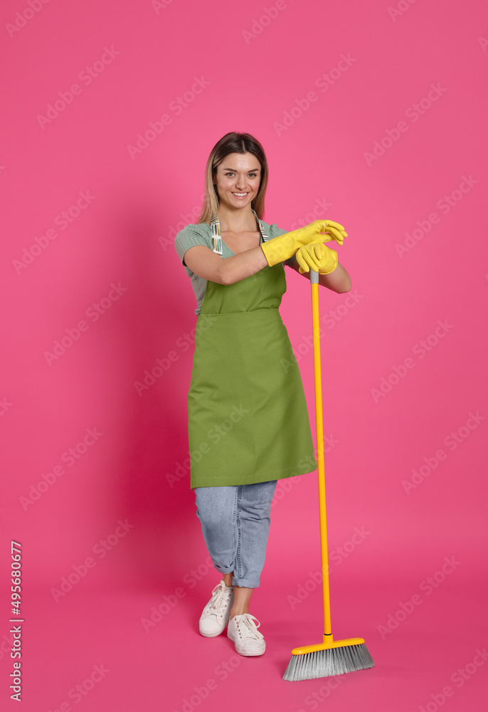 Young woman with yellow broom on pink background Young woman with yellow broom on pink background