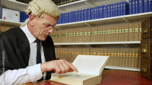 Judge or barrister reading a law book in the Judge's chambers library. The man is wearing a wig and gown with glasses.