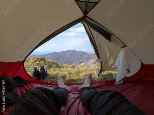 The legs and bare feet of a person in a mountain wild camping tent