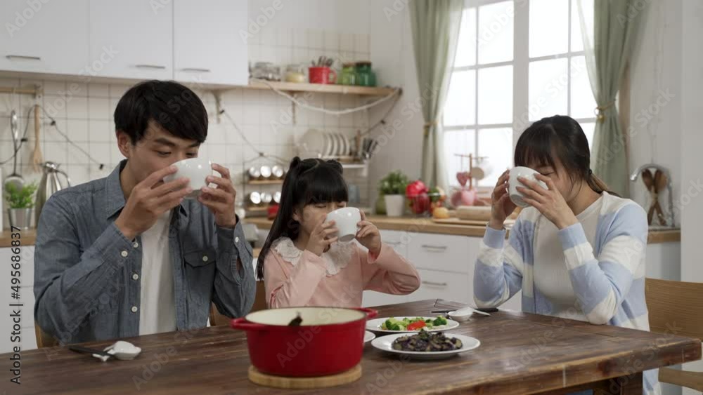 cheerful Japanese father, mother and schoolgirl daughter having bowls of delicious soup during lunch at a bright modern dining room at home cheerful Japanese father, mother and schoolgirl daughter having bowls of delicious soup during lunch at a bright modern dining room at home