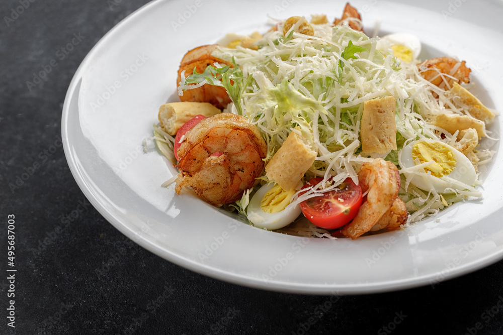 Caesar salad with shrimps, on a dark background.