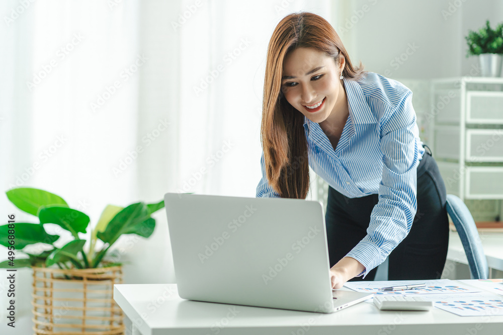 Asian business woman working on laptop standing indoor at wooden desk. Asian business woman working on laptop standing indoor at wooden desk.