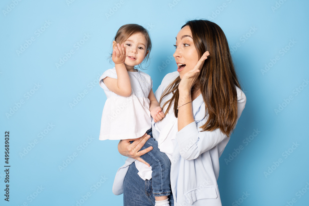 Photo of pretty young mommy hugging little daughter standing isolated over blue background. Motherhood concept. Photo of pretty young mommy hugging little daughter standing isolated over blue background. Motherhood concept.
