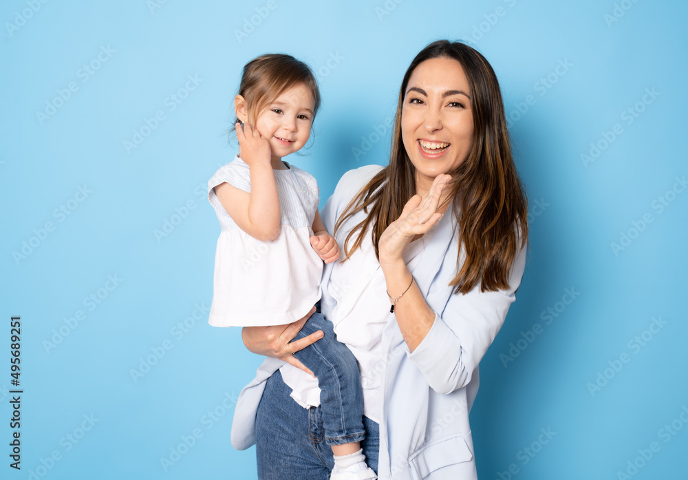 Photo of pretty young mommy hugging little daughter standing isolated over blue background. Motherhood concept. Photo of pretty young mommy hugging little daughter standing isolated over blue background. Motherhood concept.