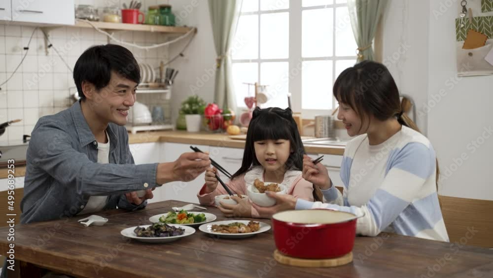 beautiful Asian family of three eating together in a modern dining room with daylight. caring father filling wife’s bowl with meat as the mother also fills daughter’s bowl with food beautiful Asian family of three eating together in a modern dining room with daylight. caring father filling wife’s bowl with meat as the mother also fills daughter’s bowl with food