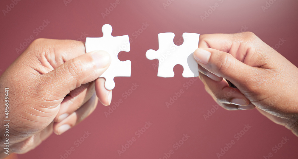 Solving the puzzle, piece by piece. Cropped shot of two unrecognizable businesspeople fitting puzzle pieces together in studio against a red background. Solving the puzzle, piece by piece. Cropped shot of two unrecognizable businesspeople fitting puzzle pieces together in studio against a red background.