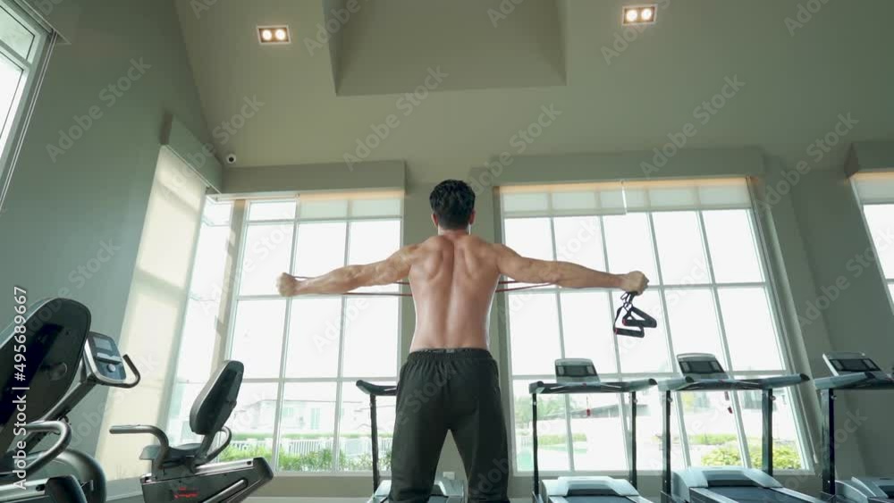Sportive man holding resistance band while training at gym training. Young man exercising with elastic weights. Sportive man holding resistance band while training at gym training. Young man exercising with elastic weights.