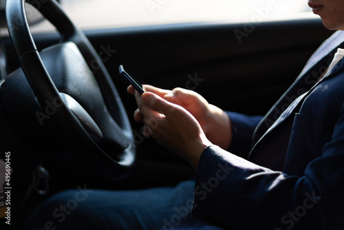 Man sitting in car using mobile phone to text while driving. Close-up of businessman while driving typing message on mobile phone. © Wasan