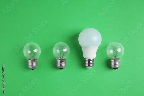 LED light bulb and simple ones on green background, flat lay. Energy saving concept