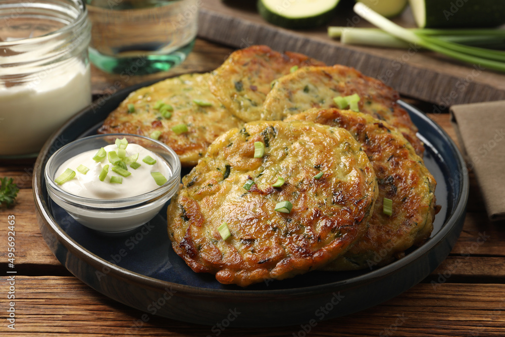 Delicious zucchini fritters with sour cream served on wooden table