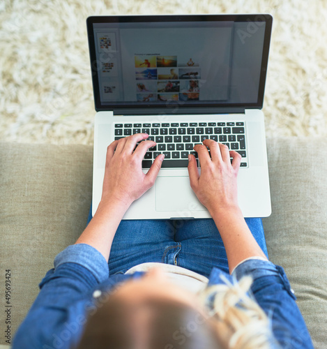 Travelling the world with her fingers. High angle shot of an unrecognizable young woman using her laptop while sitting on the sofa at home.