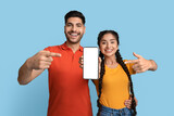 Cheerful Excited Middle Eastern Couple Pointing At Blank Smartphone Screen For Mockup