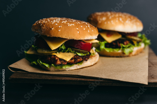 Delicious big juicy burger with tomatoes, cucumbers, cabbage, greens, cheese, cutlet on a gray background. Two sandwiches, fast food. Snack, appetizing, bun with sesame seeds. Serving in restaurant
