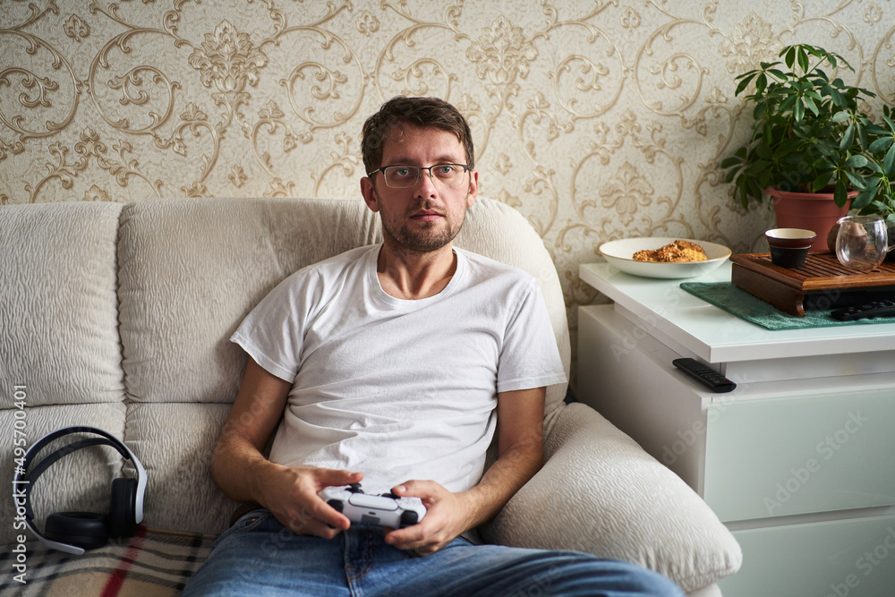 a young man plays a console sitting on the couch. holding joystick in hand