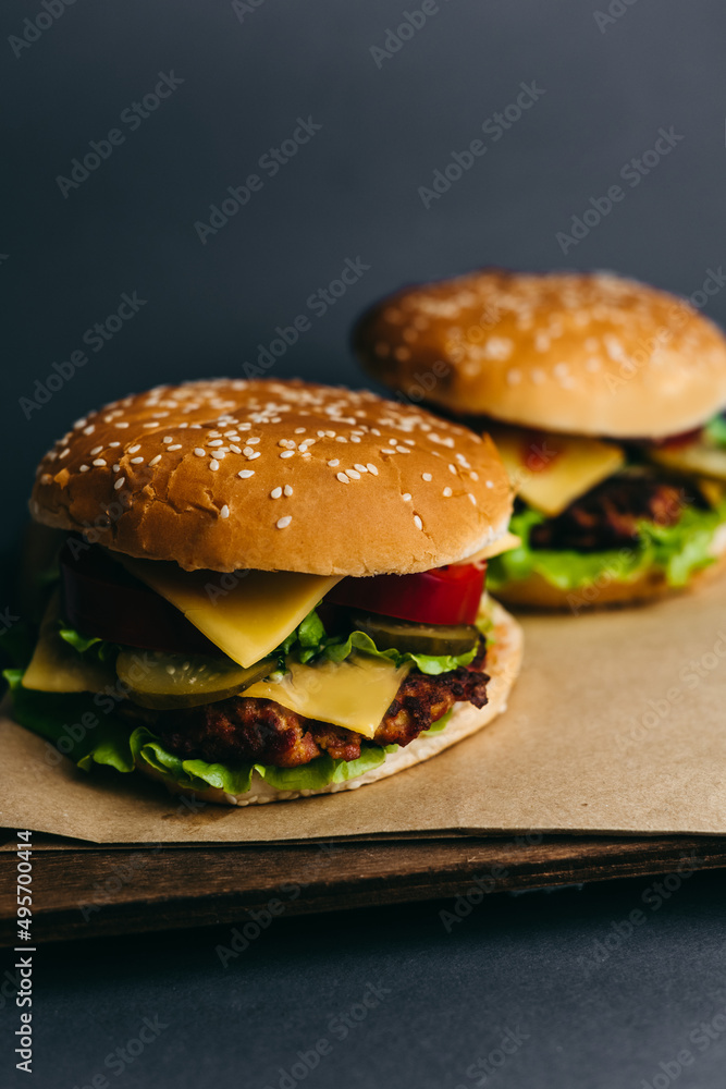 Delicious big juicy burger with tomatoes, cucumbers, cabbage, greens, cheese, cutlet on a gray background. Two sandwiches, fast food. Snack, appetizing, bun with sesame seeds. Serving in restaurant Delicious big juicy burger with tomatoes, cucumbers, cabbage, greens, cheese, cutlet on a gray background. Two sandwiches, fast food. Snack, appetizing, bun with sesame seeds. Serving in restaurant