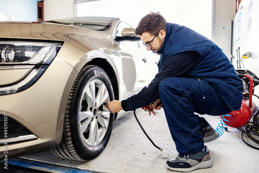 A mechanic inflates the tire on a car at workshop. A mechanic inflates the tire on a car at workshop.