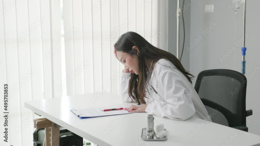 serious young asian woman doctor is writing medical document on white desk in hospital. feeling worry and hard work.... serious young asian woman doctor is writing medical document on white desk in hospital. feeling worry and hard work....