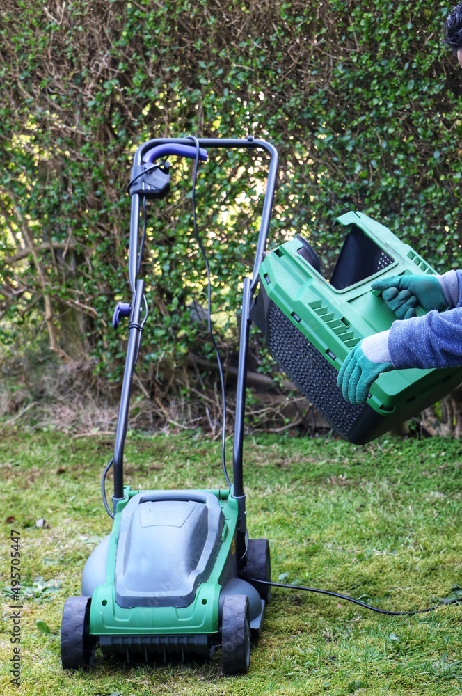 A gardener attaching the grass basket of a electric lawn mower machine A gardener attaching the grass basket of a electric lawn mower machine