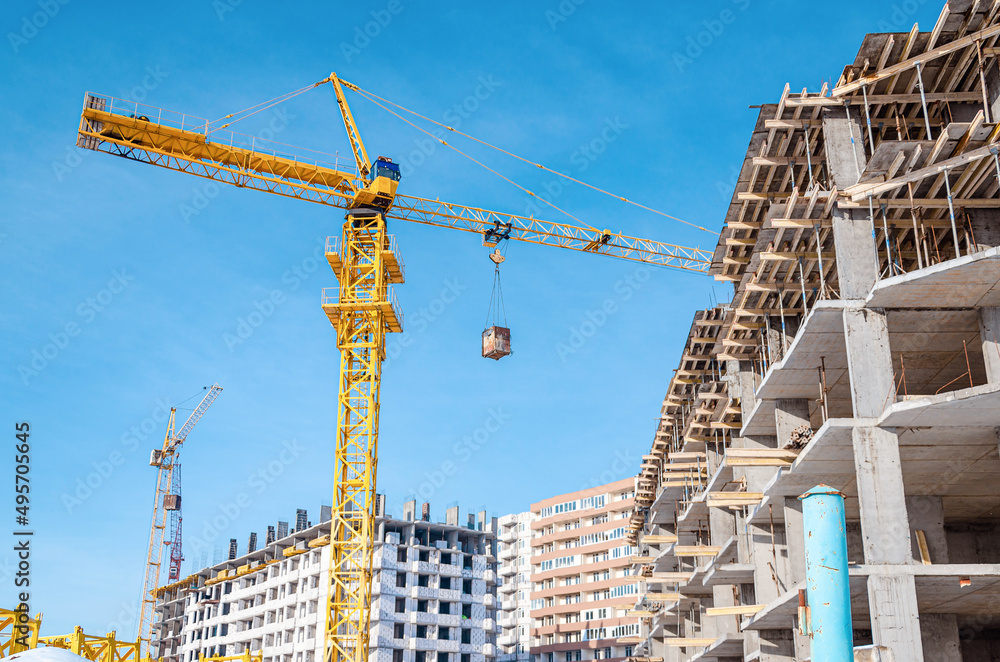 Construction of a multi-storey building. Yellow and blue cranes. Cargo transfer. Sunlight on the construction site. Construction of a multi-storey building. Yellow and blue cranes. Cargo transfer. Sunlight on the construction site.