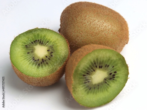 One whole kiwi and a second kiwi cut in half. Close-up, light gray background, selective focus.