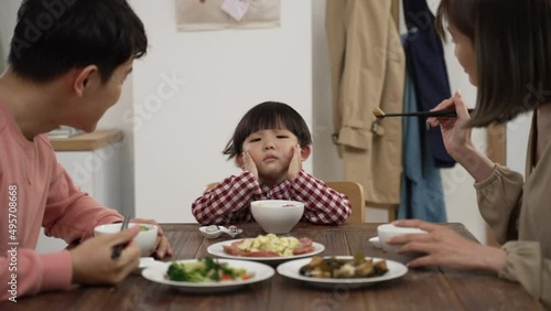 closeup of unhappy Asian preschool boy shaking head and saying no to eat at dining table to his mom and dad at home