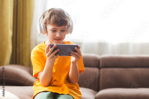 kid use the phone, play the game. teenager in headphones plays on a smartphone or watches video sitting on the couch at home