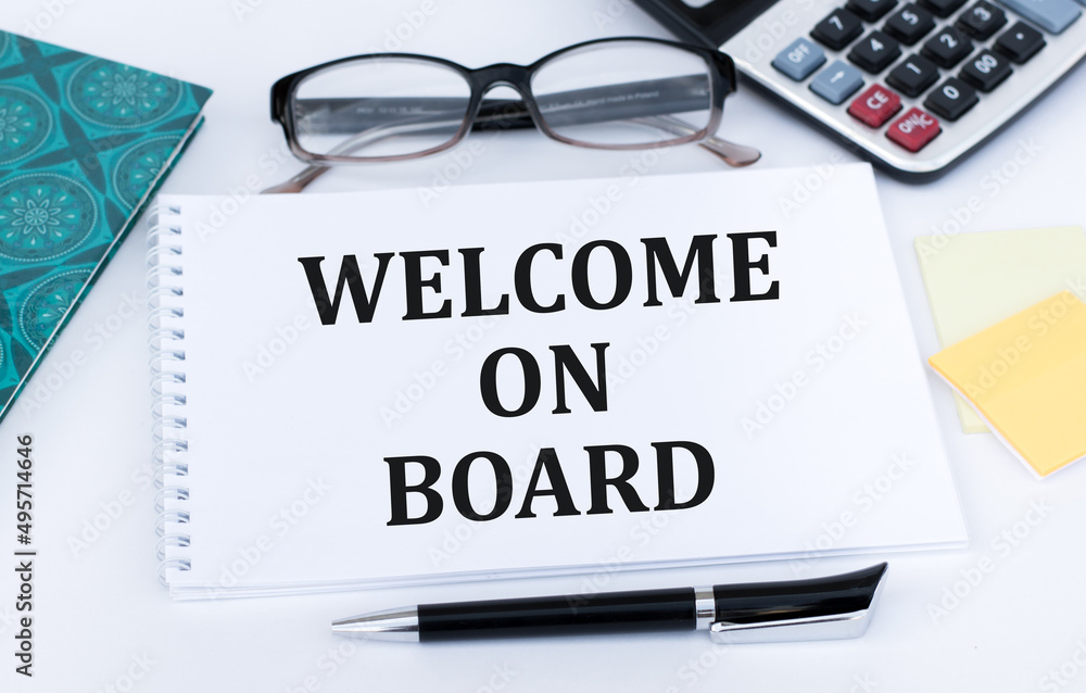 Welcome on board inscription on notepad on the table next to pen, calculator, glasses and documents Welcome on board inscription on notepad on the table next to pen, calculator, glasses and documents