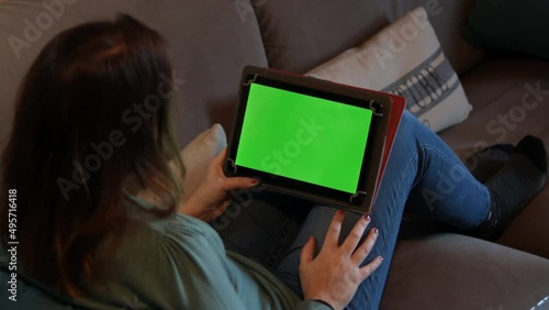 Girl sitting on the sofa at home holding a tablet with green screen.  Watching entertainment content or learning.  