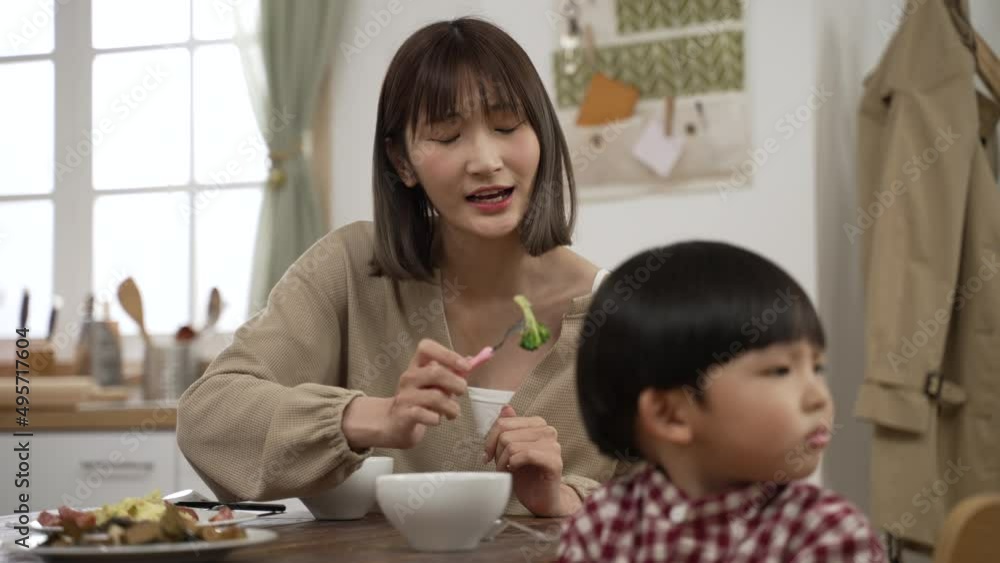 selective focus frustrated Asian mother holding a fork with vegetable and asking his baby son to take a bite in dining room at home. the boy turns head away and refuses to eat selective focus frustrated Asian mother holding a fork with vegetable and asking his baby son to take a bite in dining room at home. the boy turns head away and refuses to eat