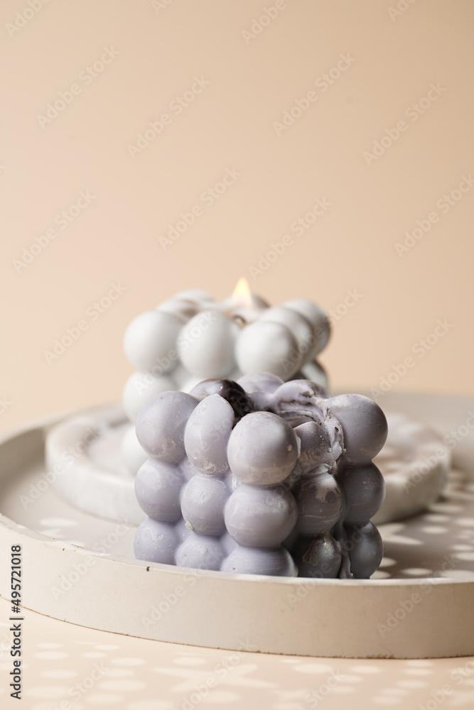 Two grey bubble candles on gray concrete tray on beige colored seamless surface with starry light shadows Two grey bubble candles on gray concrete tray on beige colored seamless surface with starry light shadows