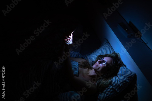 Pretty, middle-aged woman using her cell phone in bed at night - unhealthy blue light exposure