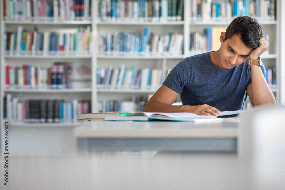 Students in a library - handsome student reading a book for his class in a bright modern library Students in a library - handsome student reading a book for his class in a bright modern library