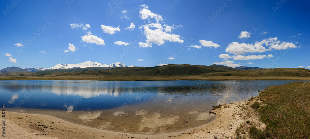 panorama of the river on the Ukok plateau with the reflection in the water of the mountain complex of the Tabyn-Bogdo-Ola glacier and the blue sky with clouds panorama of the river on the Ukok plateau with the reflection in the water of the mountain complex of the Tabyn-Bogdo-Ola glacier and the blue sky with clouds