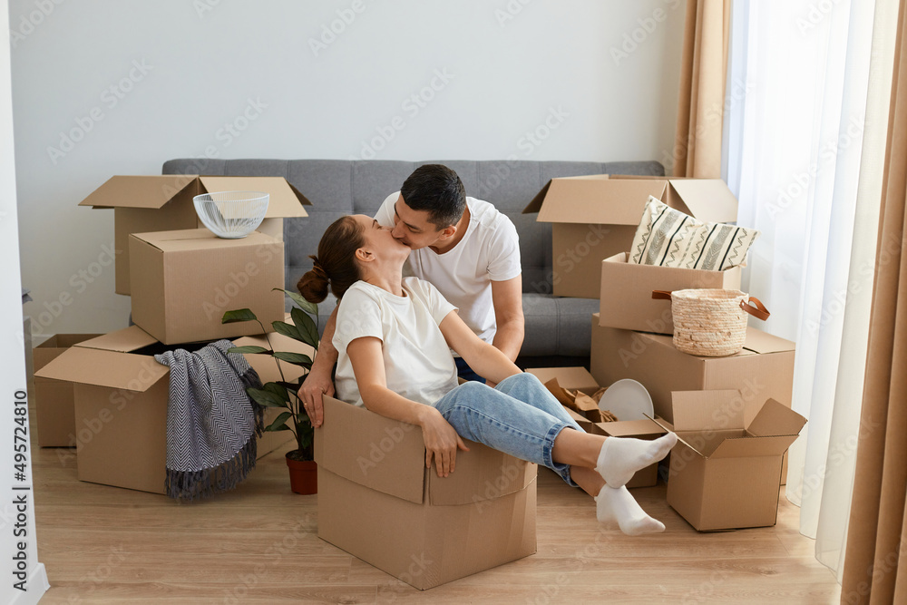 Portrait of happy romantic couple having fun while moving into new house, attractive woman sitting in cardboard box while man kissing her with love na gentle. Portrait of happy romantic couple having fun while moving into new house, attractive woman sitting in cardboard box while man kissing her with love na gentle.