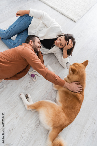 top view of happy young couple looking at each other while lying of floor with akita inu dog.