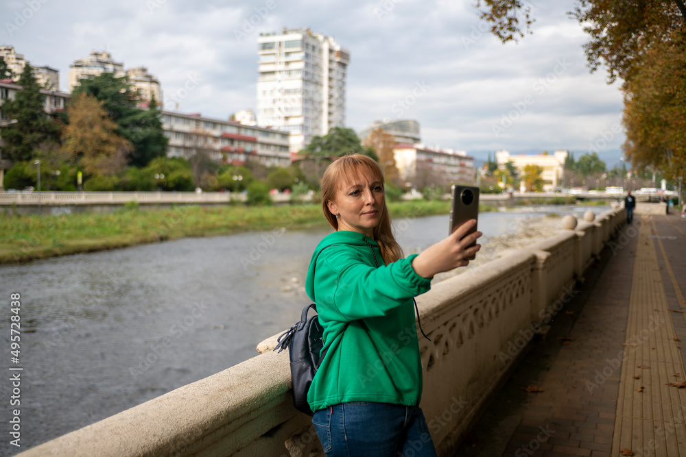 The girl takes a selfie at the parapet against the background of the river.