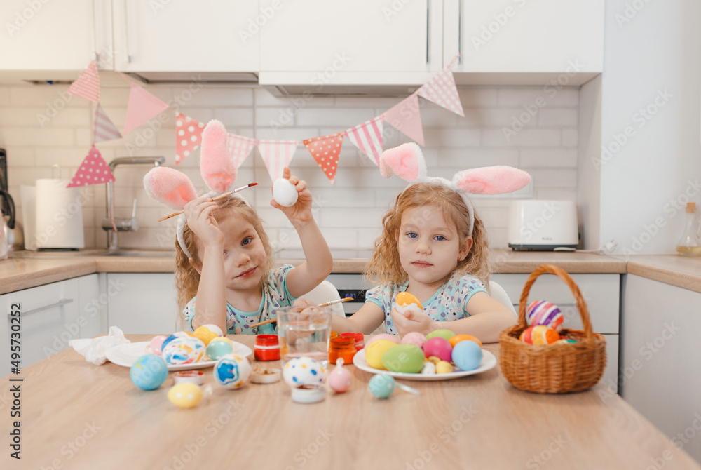 two twin girls are preparing for the Easter holiday at the kitchen table painting Easter eggs. two twin girls are preparing for the Easter holiday at the kitchen table painting Easter eggs.