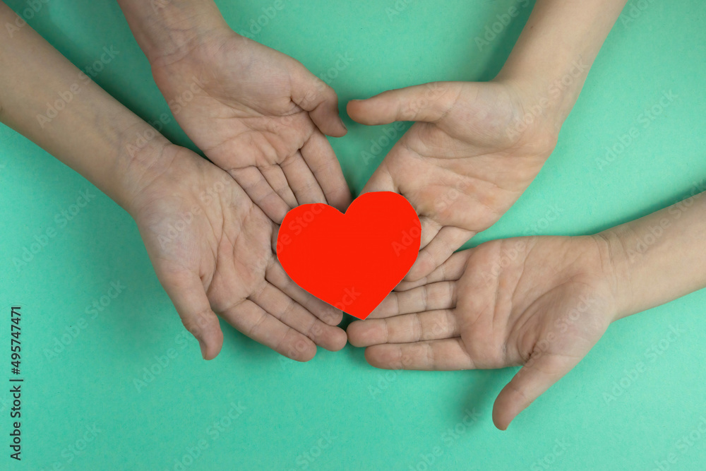 Close-up of children's hands holding a red heart cut out of paper. Children's love and friendship theme. Valentine's Day, children's gift. Mother's day Close-up of children's hands holding a red heart cut out of paper. Children's love and friendship theme. Valentine's Day, children's gift. Mother's day