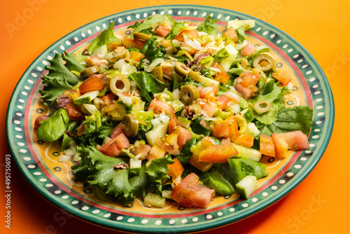 Detalhe de prato com salada de vegetais sobre superfície alaranjada.