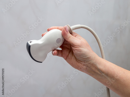 The doctor holds an ultrasound probe in his hands. On a gray background.