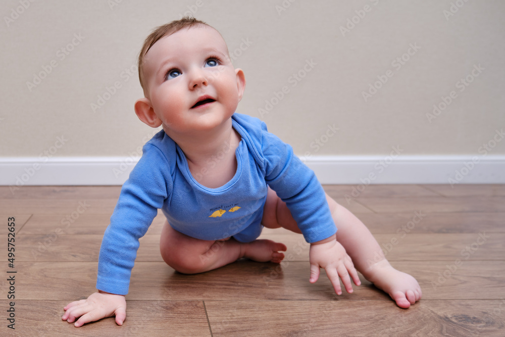 Happy baby toddler crawls on a wooden laminate. Funny child is sitting smiling on the parquet in the home living room, aged 6-11 months Happy baby toddler crawls on a wooden laminate. Funny child is sitting smiling on the parquet in the home living room, aged 6-11 months