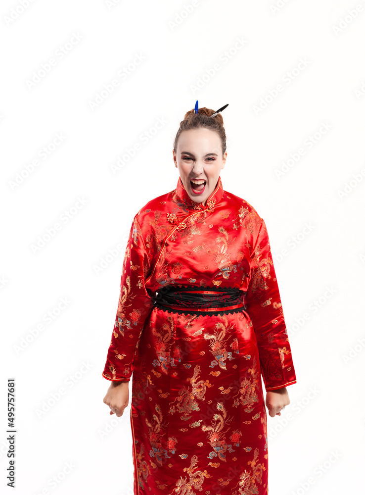 young woman in red oriental costume, looking directly at the camera, shouting and clenching his fists with his arms outstretched against a white background. young woman in red oriental costume, looking directly at the camera, shouting and clenching his fists with his arms outstretched against a white background.