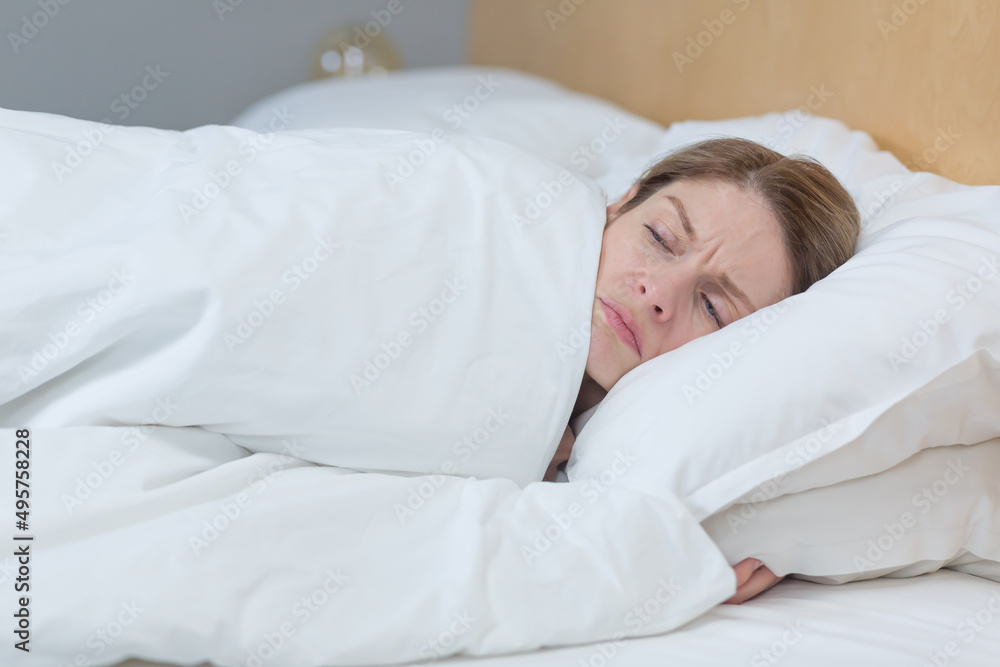 Close-up photo of a sleepless and upset woman lying in bed under a blanket, trying to fall asleep Close-up photo of a sleepless and upset woman lying in bed under a blanket, trying to fall asleep