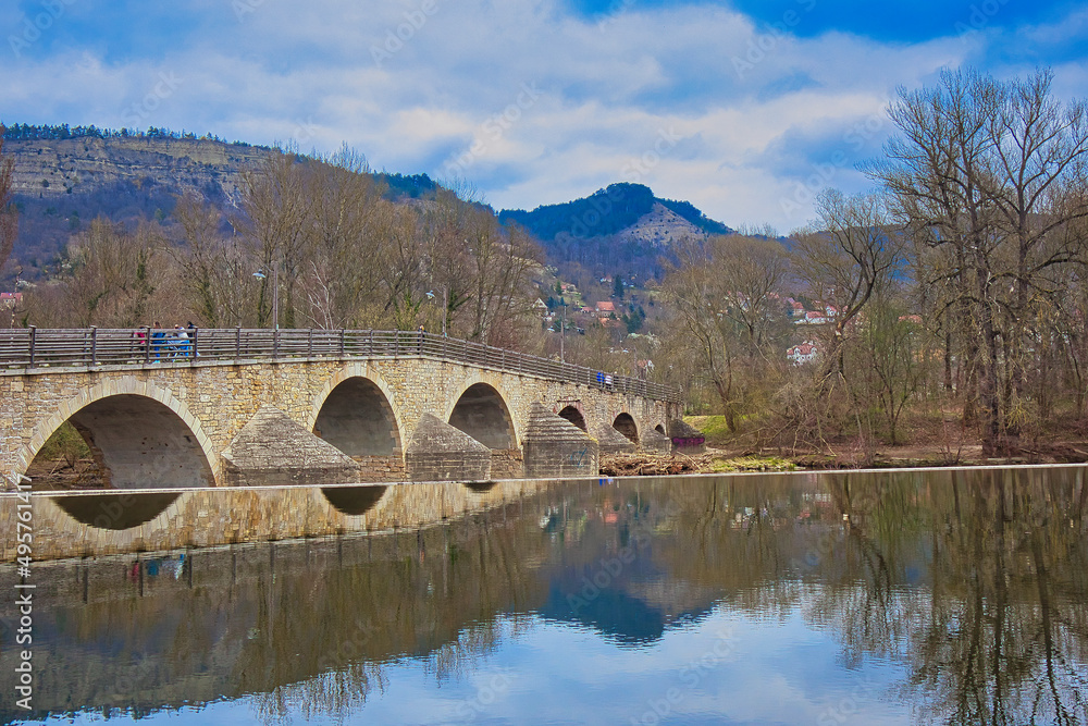 Fototapeta premium Historische Steinbogenbrücke über die Saale mit Spiegelung im Wasser und Blick auf die Kernberge, Alte Burgauer Brücke als Baudenkmal, Jena, Kreisfreie Stadt Jena, Thüringen, Deutschland