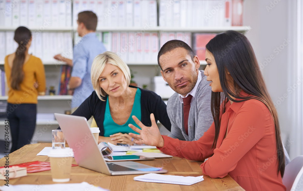 We have to come up with a solution. Three coworkers brainstorming around a laptop while their colleagues read files in the background. We have to come up with a solution. Three coworkers brainstorming around a laptop while their colleagues read files in the background.