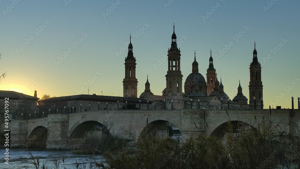 Panoramic view of the stone bridge and the Basilica del Pilar at sunset in Zaragoza, Spain.