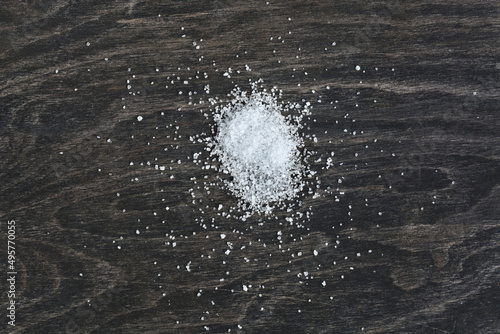 Pile of scattered white salt on a kitchen board. Copy space on a dark background.