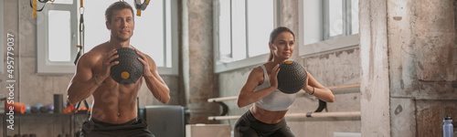 Concentrated sporty man and woman with athletic bodies working out with exercise balls in gym club