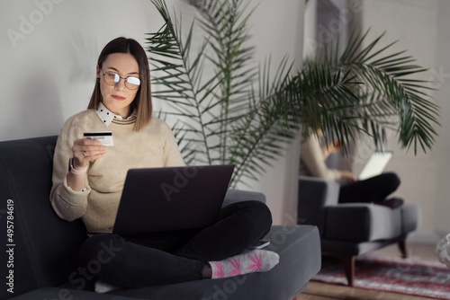 Online shopping using card and laptop. Caucasian woman using technology to shop while sitting on a sofa indoors